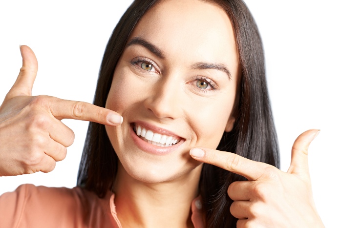 Woman pointing her smile after cosmetic dental treatment at Portage Northern Dental in Michigan